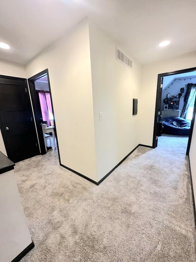 hallway featuring light carpet, baseboards, and visible vents