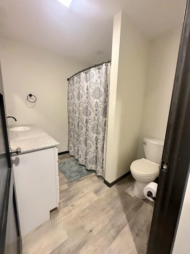 bathroom featuring curtained shower, toilet, wood finished floors, vanity, and baseboards