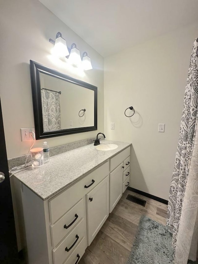 bathroom with visible vents, vanity, baseboards, and wood finished floors