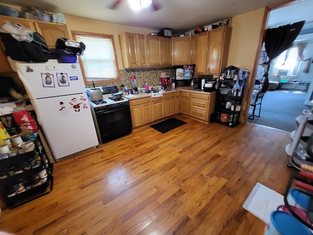 kitchen with black range oven, white fridge, light hardwood / wood-style flooring, and tasteful backsplash