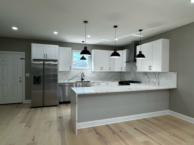 kitchen with light wood-type flooring, light stone countertops, stainless steel appliances, wall chimney range hood, and kitchen peninsula