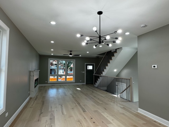 unfurnished living room featuring ceiling fan with notable chandelier and light hardwood / wood-style flooring