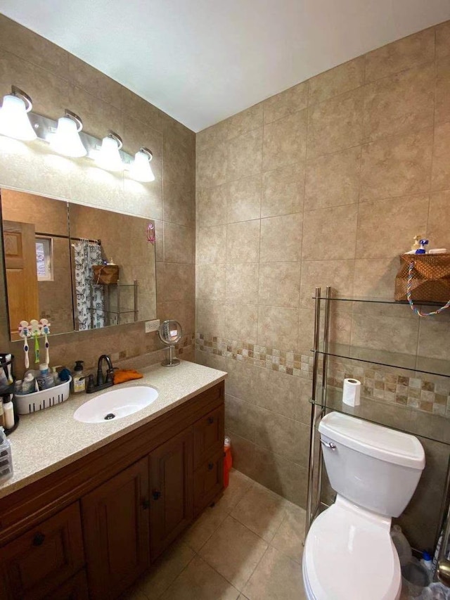 bathroom with tile walls, toilet, vanity, and tile patterned floors