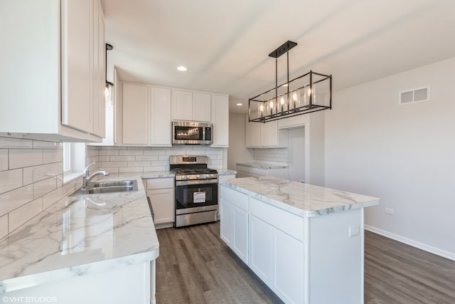 kitchen with white cabinets, a kitchen island, sink, decorative light fixtures, and stainless steel appliances