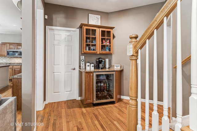 bar with light stone countertops, light hardwood / wood-style flooring, wine cooler, and decorative backsplash