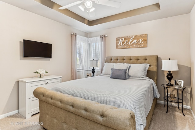 bedroom featuring a raised ceiling, ceiling fan, and light carpet