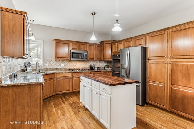 kitchen with butcher block counters, a center island, hanging light fixtures, appliances with stainless steel finishes, and light hardwood / wood-style floors