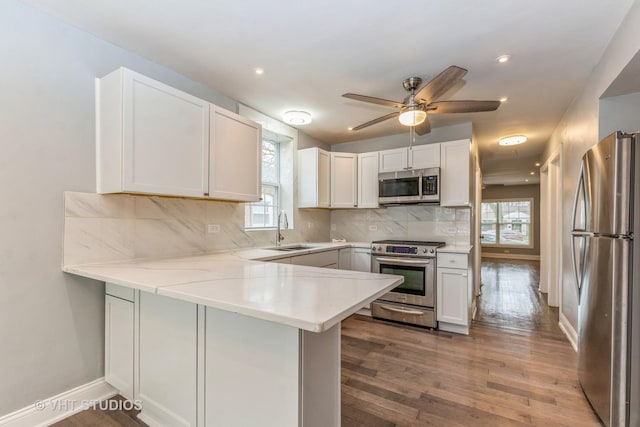 kitchen with kitchen peninsula, tasteful backsplash, stainless steel appliances, sink, and white cabinetry