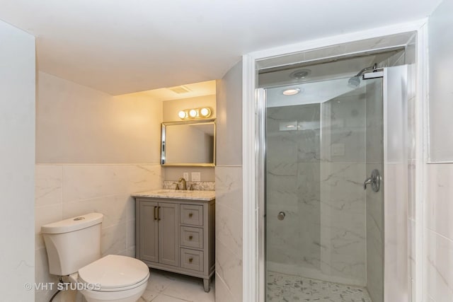 bathroom with vanity, toilet, a shower with shower door, and tile walls