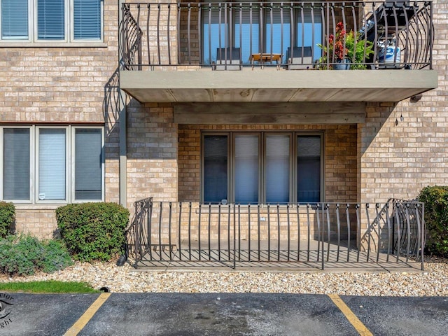 view of exterior entry with uncovered parking, brick siding, and a balcony