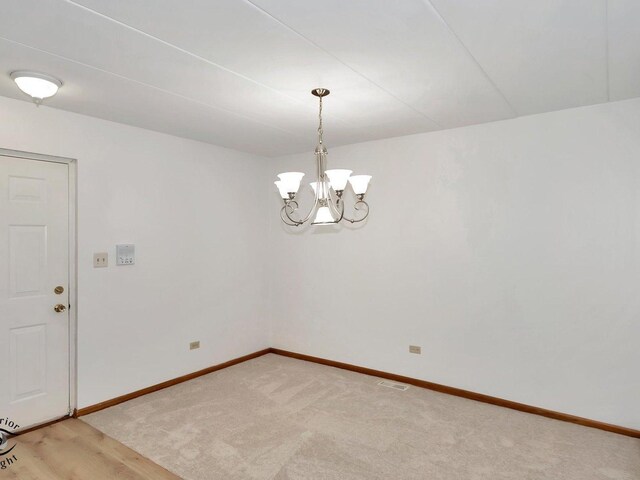 carpeted spare room featuring an inviting chandelier