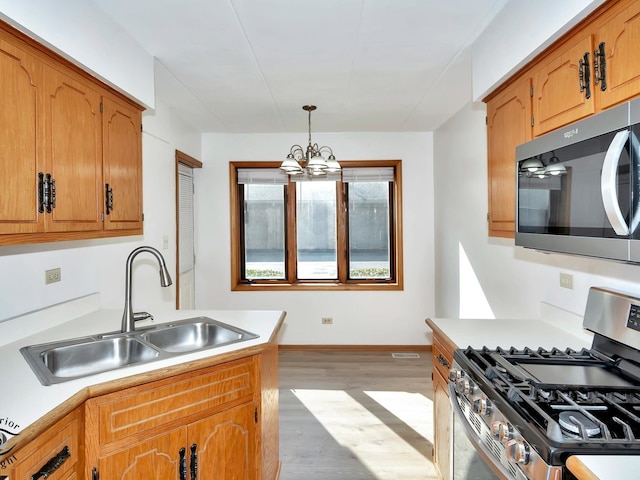 kitchen with hanging light fixtures, an inviting chandelier, light wood-type flooring, stainless steel appliances, and sink