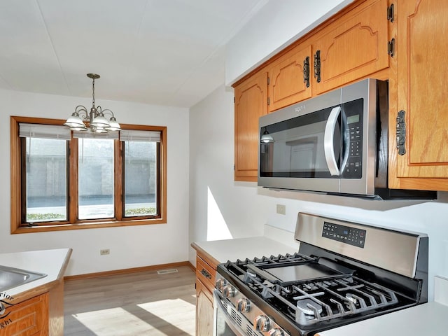 kitchen with pendant lighting, light hardwood / wood-style flooring, a notable chandelier, stainless steel appliances, and sink