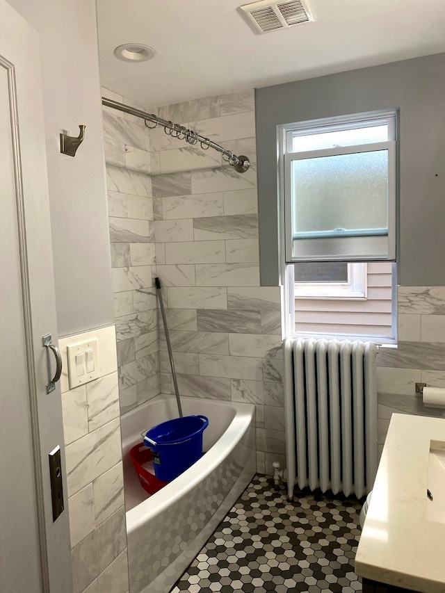 bathroom featuring radiator, tile walls, vanity, tiled shower / bath combo, and tile patterned floors