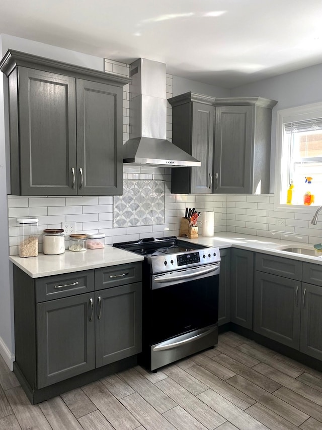 kitchen with light hardwood / wood-style floors, wall chimney range hood, sink, and stainless steel range