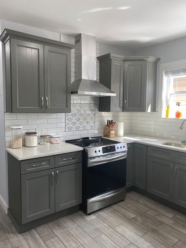 kitchen with light hardwood / wood-style flooring, wall chimney range hood, sink, and stainless steel range