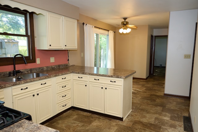 kitchen featuring baseboards, a ceiling fan, a peninsula, white cabinetry, and a sink