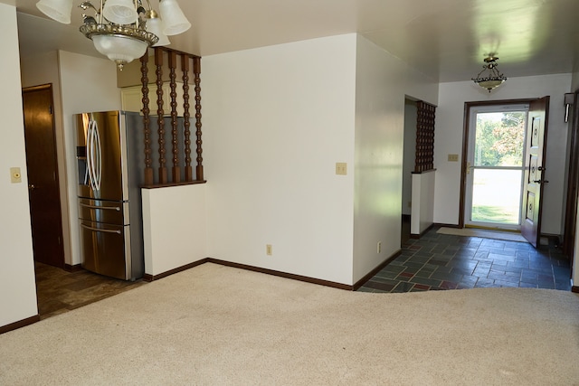 entryway featuring an inviting chandelier, carpet, stone tile flooring, and baseboards