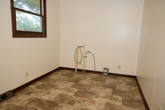 clothes washing area featuring visible vents, baseboards, laundry area, and stone finish flooring