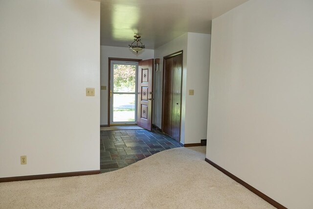 entryway with dark carpet, baseboards, and stone tile floors