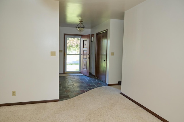 entryway featuring stone tile floors, baseboards, and dark carpet