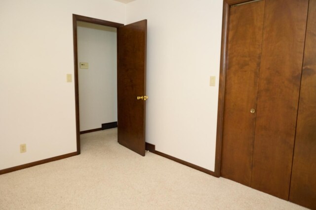 unfurnished bedroom with baseboards, a closet, and light colored carpet