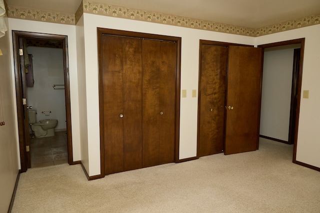 unfurnished bedroom featuring baseboards, light carpet, ensuite bath, and two closets