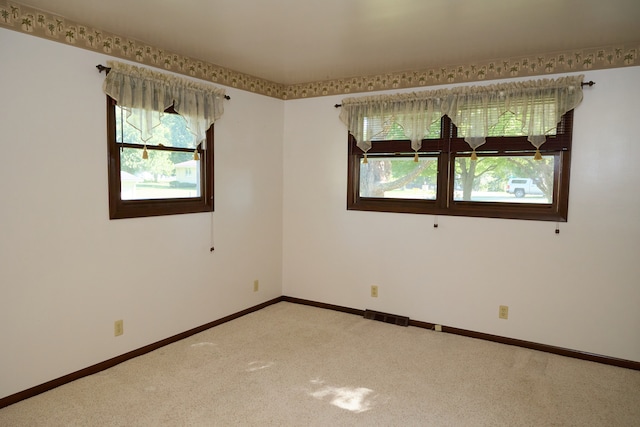 empty room featuring light carpet, visible vents, and baseboards