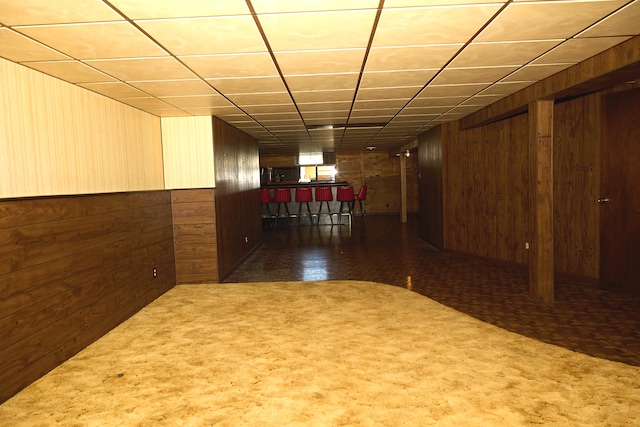 finished basement with a wainscoted wall, a bar, wood walls, and carpet flooring