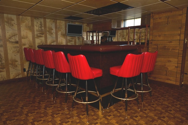 bar with a dry bar, wooden walls, and a paneled ceiling