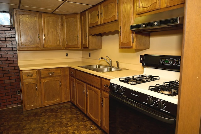 kitchen featuring a sink, under cabinet range hood, gas range oven, brown cabinetry, and light countertops