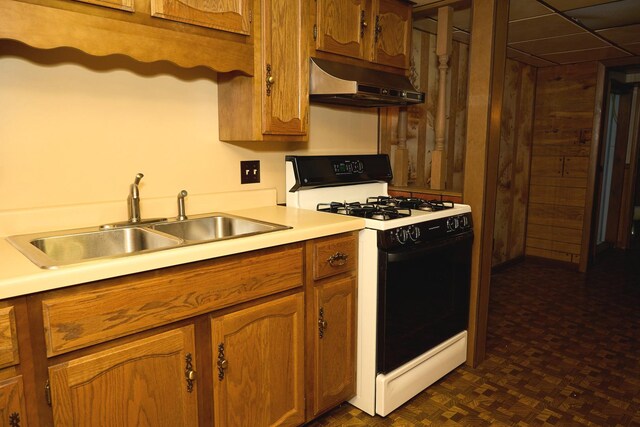 kitchen featuring brown cabinets, under cabinet range hood, a sink, range with gas cooktop, and light countertops