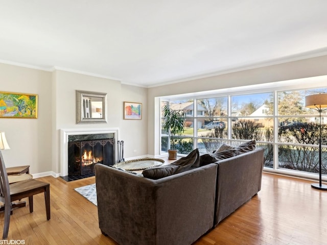 living room featuring a healthy amount of sunlight, ornamental molding, a high end fireplace, and light hardwood / wood-style flooring