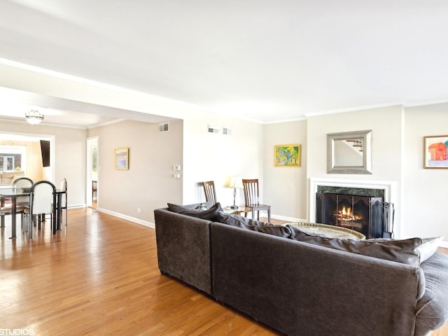 living room with crown molding, a high end fireplace, and light hardwood / wood-style floors