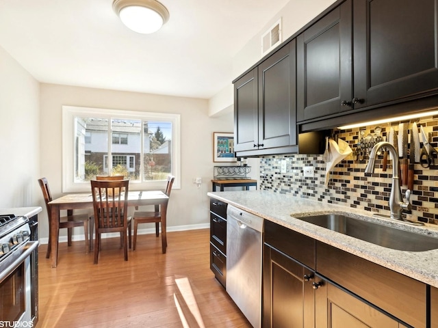 kitchen with appliances with stainless steel finishes, tasteful backsplash, light stone counters, sink, and light hardwood / wood-style flooring