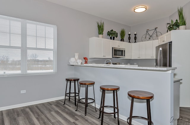 kitchen featuring a kitchen bar, stainless steel appliances, wood-type flooring, and kitchen peninsula