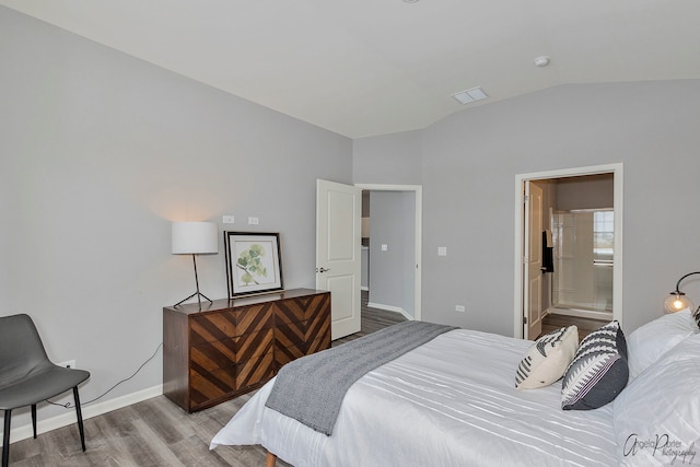 bedroom featuring lofted ceiling, light hardwood / wood-style flooring, and connected bathroom