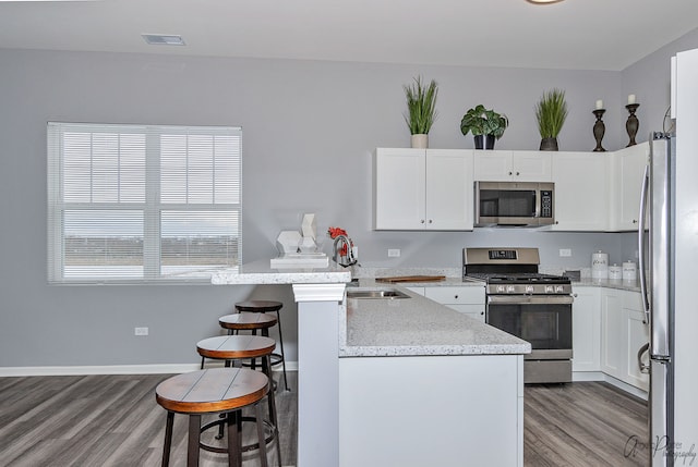 kitchen featuring light stone counters, hardwood / wood-style floors, appliances with stainless steel finishes, and white cabinets