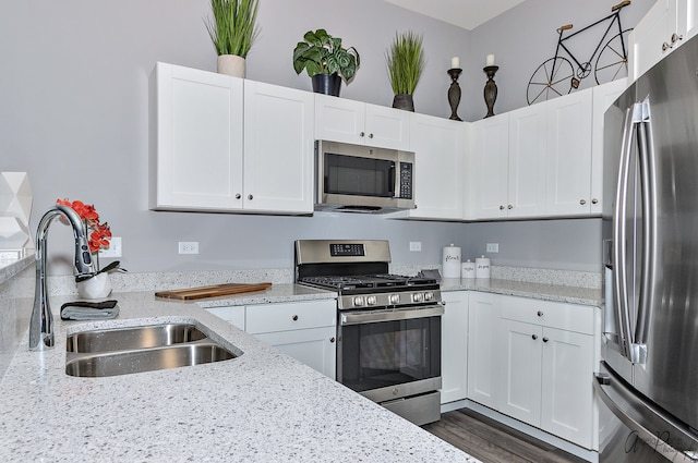 kitchen with appliances with stainless steel finishes, dark wood-type flooring, sink, light stone counters, and white cabinets