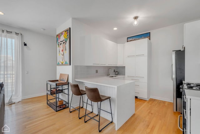 kitchen featuring white cabinetry, sink, light hardwood / wood-style flooring, and a breakfast bar