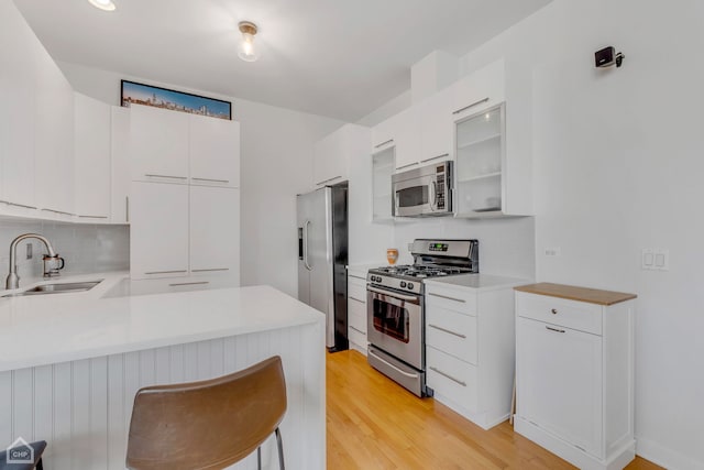 kitchen with white cabinets, sink, kitchen peninsula, light hardwood / wood-style flooring, and stainless steel appliances