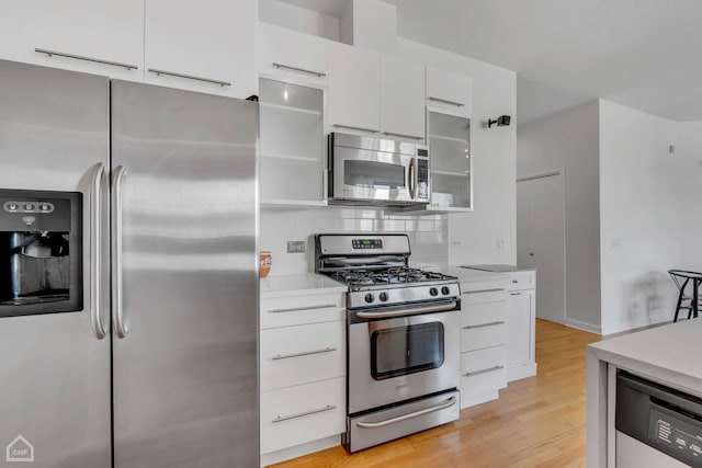 kitchen with appliances with stainless steel finishes, white cabinetry, light hardwood / wood-style flooring, and tasteful backsplash