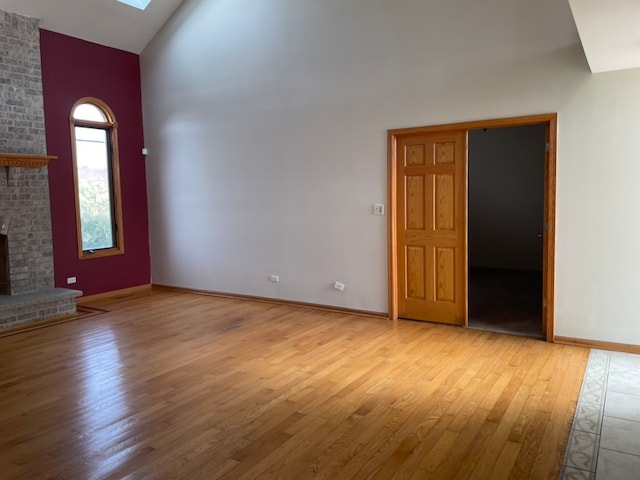 unfurnished living room with vaulted ceiling, light hardwood / wood-style floors, and a brick fireplace