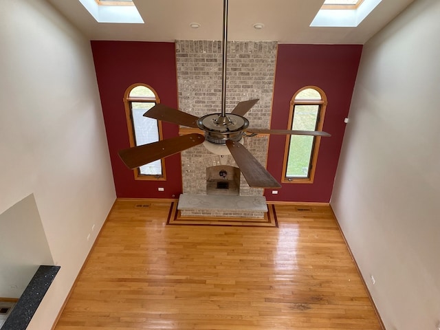 unfurnished living room with a wealth of natural light, light hardwood / wood-style flooring, ceiling fan, and vaulted ceiling with skylight