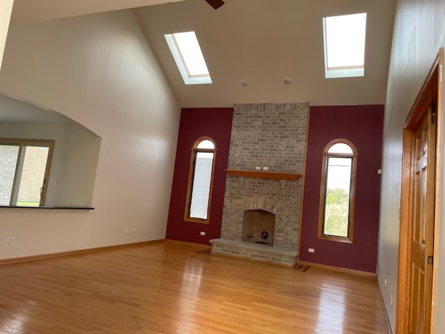 unfurnished living room featuring light hardwood / wood-style floors, high vaulted ceiling, a skylight, and a fireplace