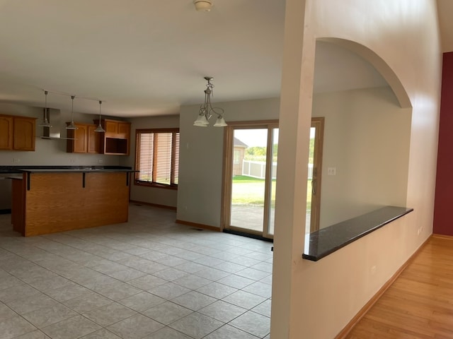 kitchen with light hardwood / wood-style floors, a kitchen bar, hanging light fixtures, a chandelier, and wall chimney range hood