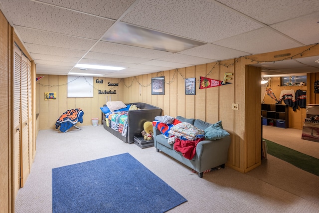 rec room with a paneled ceiling, wood walls, and carpet floors