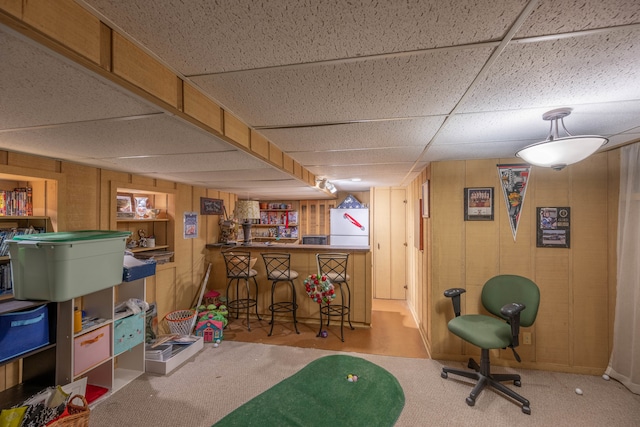 game room featuring indoor bar, light colored carpet, a drop ceiling, and wooden walls