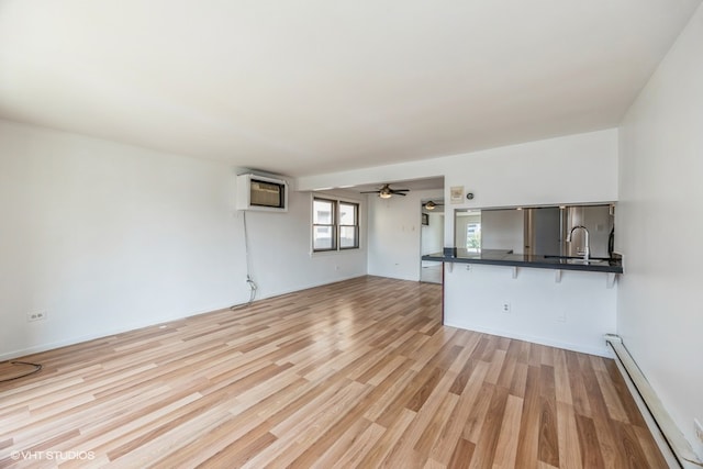 unfurnished living room with a wall unit AC, a baseboard heating unit, light hardwood / wood-style floors, sink, and ceiling fan