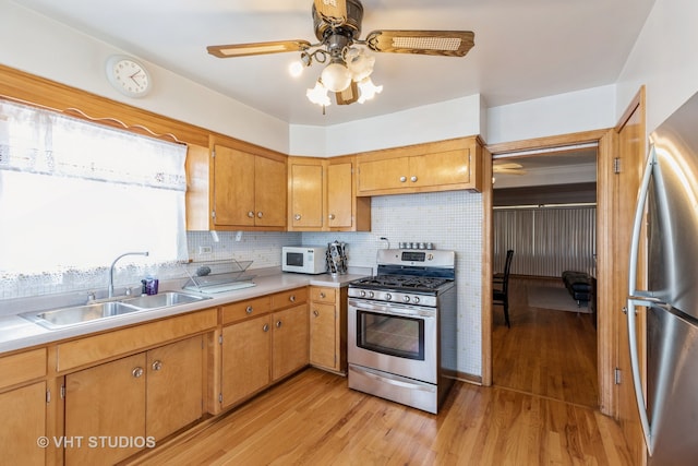 kitchen featuring backsplash, stainless steel appliances, light hardwood / wood-style floors, sink, and ceiling fan